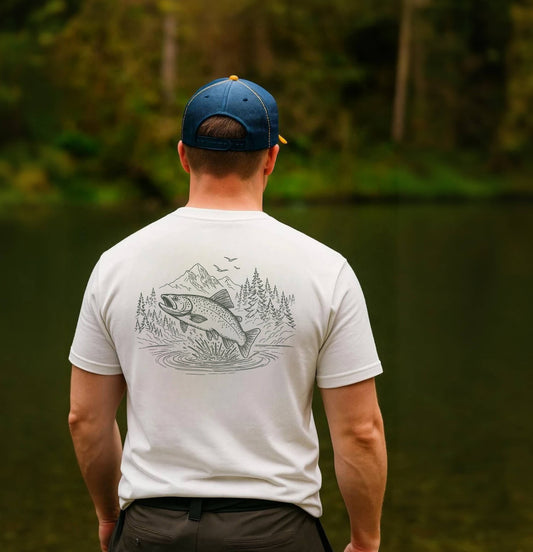 Man wearing a white t-shirt with a fish graphic, standing by a body of water with trees in the background.