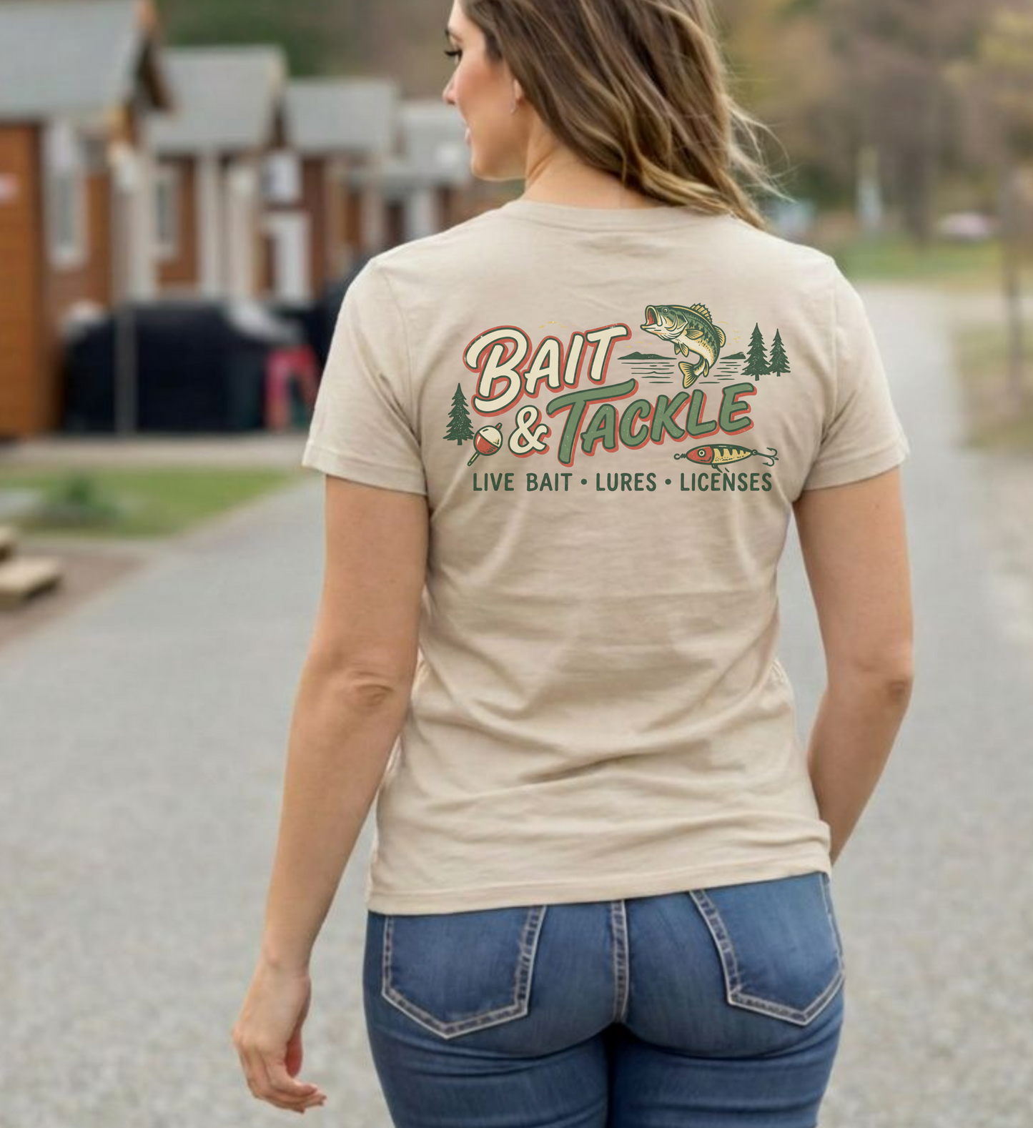 Woman wearing a beige t-shirt with 'Bait & Tackle' graphic design outdoors.