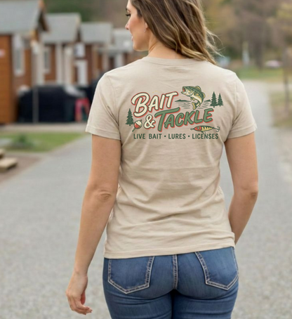Woman wearing a beige t-shirt with 'Bait & Tackle' graphic design outdoors.
